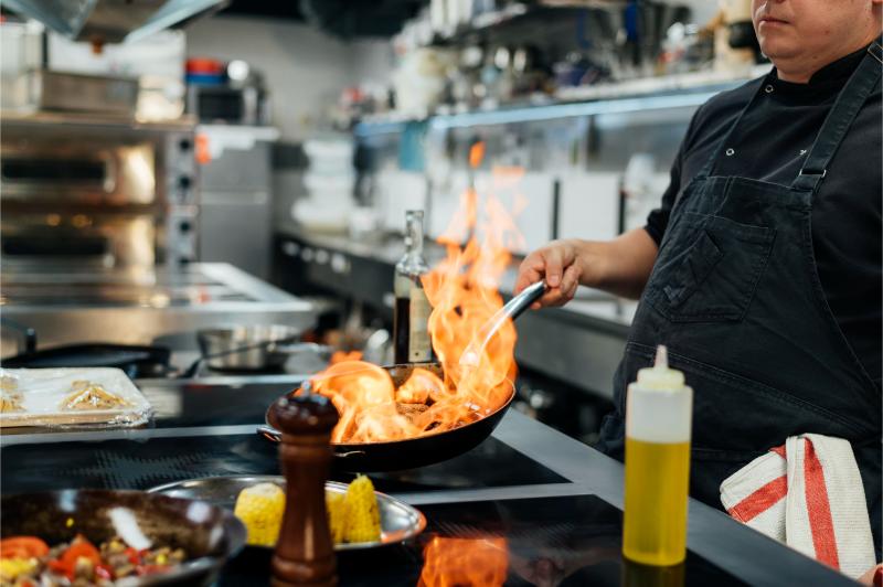 vista lateral plato flameado chef masculino en cocina de un restaurante